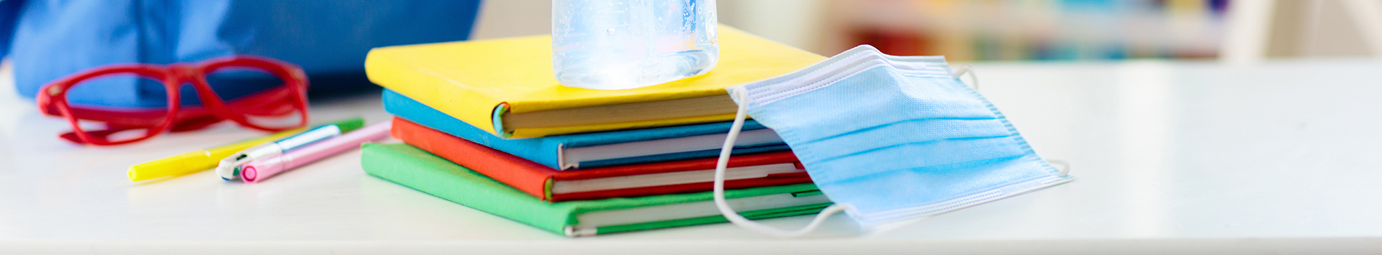 Child's backpack on table with books, glasses, and face mask